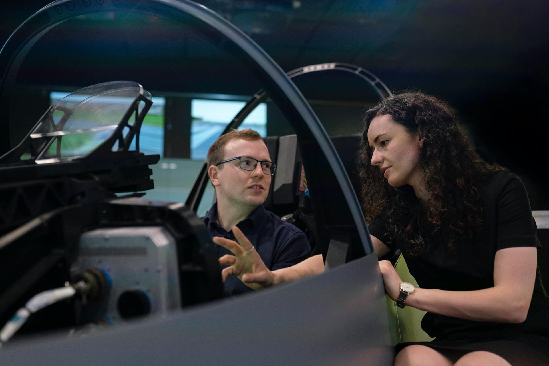 Engineers in a dark simulation lab inspecting cockpit hardware and wiring on a test rig