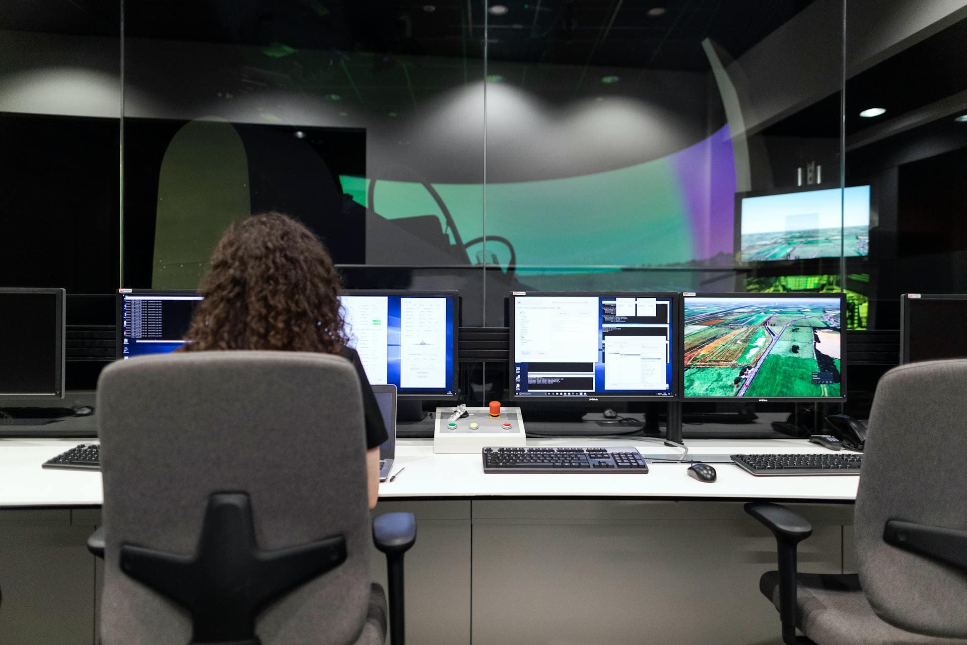 A student at a multi-monitor engineering workstation with maps, telemetry, and control hardware